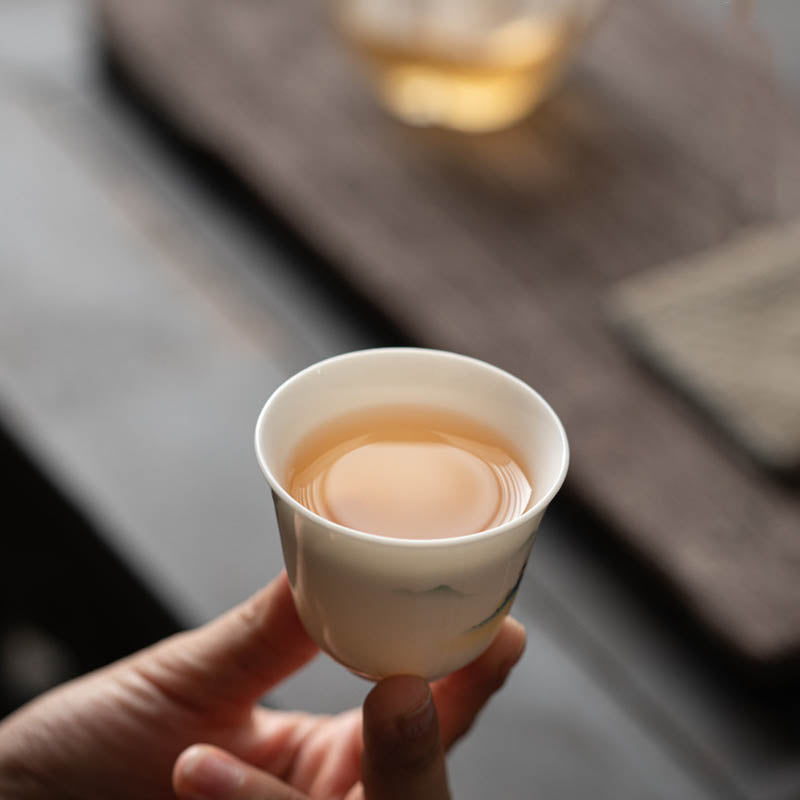 Ceramic Kung Fu Tea Cup – cradled by two hands, blue mountain scene with pavilion, intimate tea moment, reverent