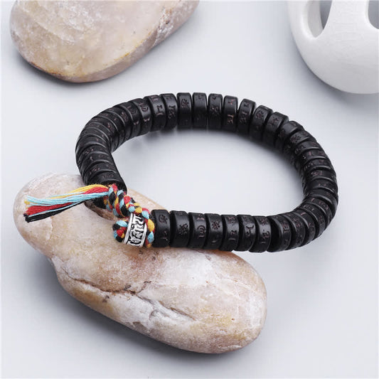 Coconut Shell Mantra Bracelet - Resting on natural river stone, black mantra beads with woven cord closure