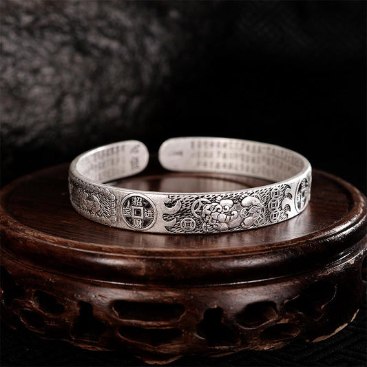 Antique silver Pixiu bracelet on dark carved wooden stand, featuring mythical wealth beast, lucky coin motifs and Buddhist scripture engraving