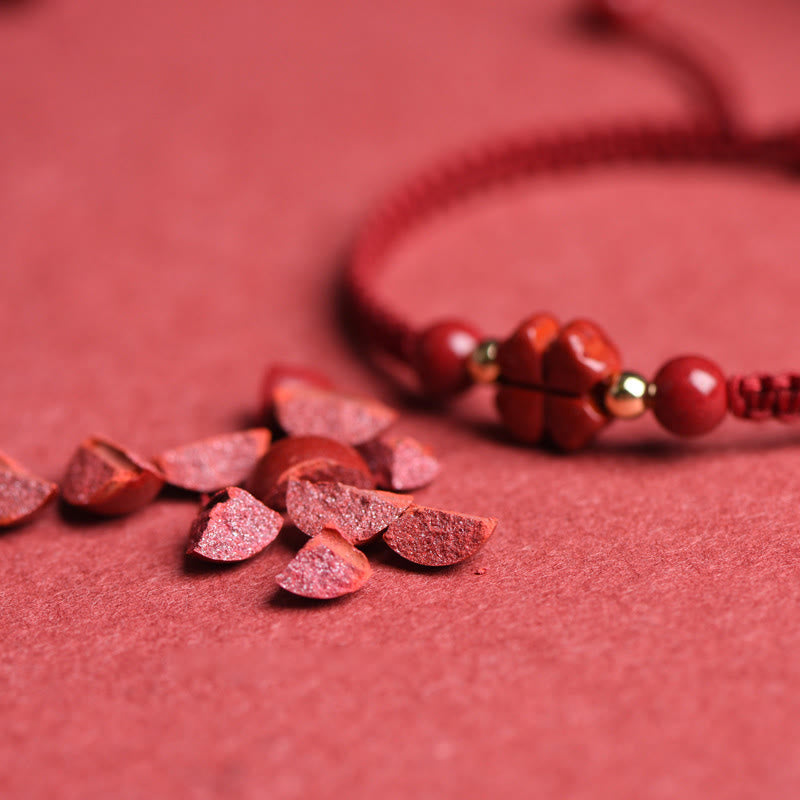 Red cinnabar flower charm bracelet with gold accent beads on braided red cord, macro close-up showing carved five-petal flower on matching red background