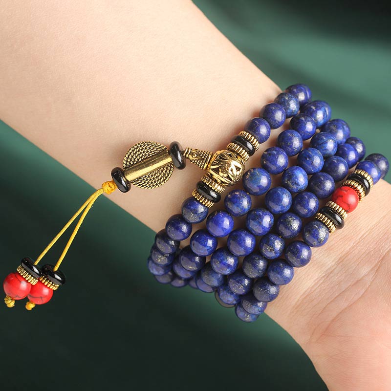 Lapis Lazuli Red Turquoise Tibetan Mala Bracelet worn on wrist, 108 royal blue lapis beads four-wrap style, gold guru bead with carved detail, red coral markers, yellow gold tassel with red beads, lifestyle wrist shot