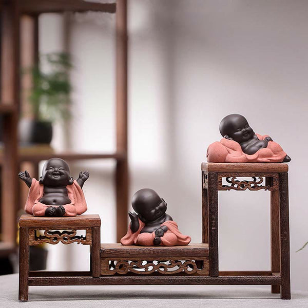 Laughing Buddha Purple Clay Maitreya Statue – low-angle seated figure in sage green robe, matte dark brown skin, wood-grain surface, minimalist zen styling