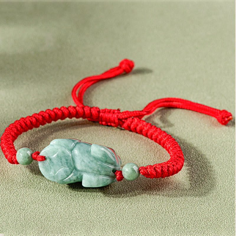 Jade PiXiu Knot Bracelet – Red braided cord bracelet with jade PiXiu from side angle on beige fabric