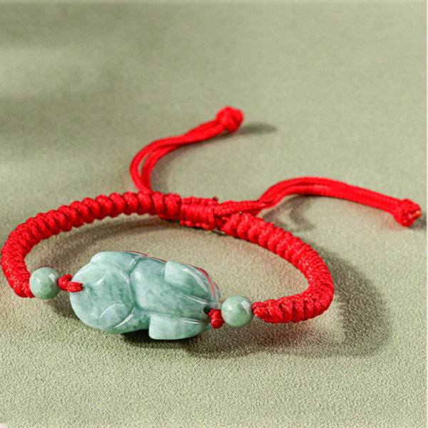 Jade PiXiu Knot Bracelet – Red braided cord bracelet with jade PiXiu from side angle on beige fabric