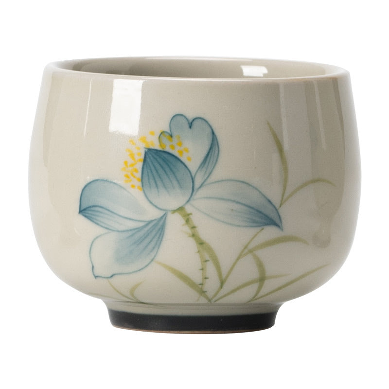 Hand Painted Lotus Tea Cup – three-quarter view on white, blue lotus with stems and leaves, dark foot ring, studio