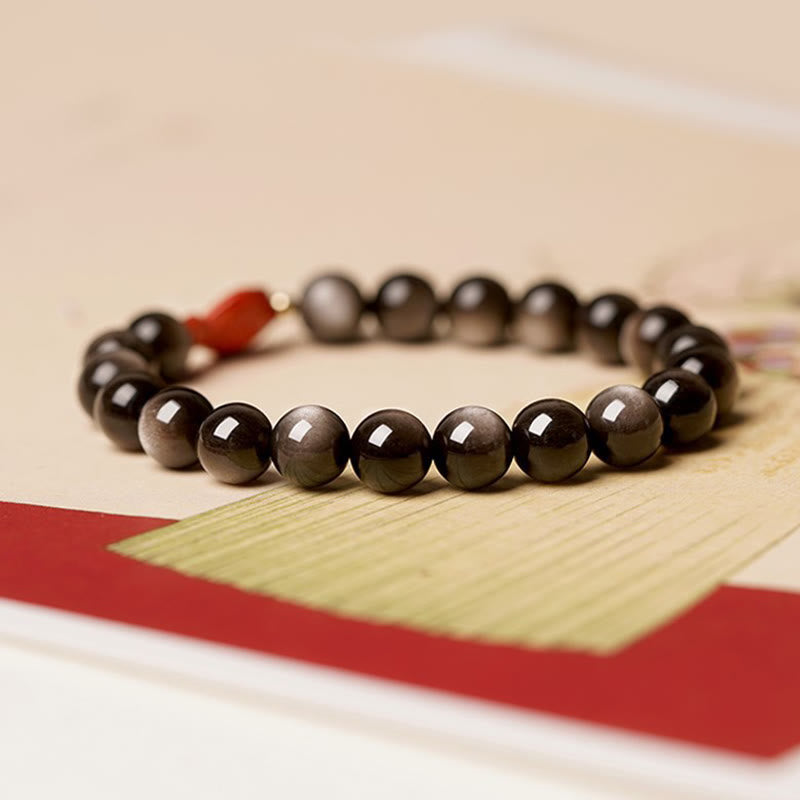 Silver Sheen Obsidian Bracelet – flat lay on dark surface, koi fish charm, cinnabar and obsidian