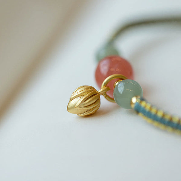 Red Agate Jade Lotus Bracelet – gold lotus bud charm with pink and green beads on teal cord, macro side-angle close-up