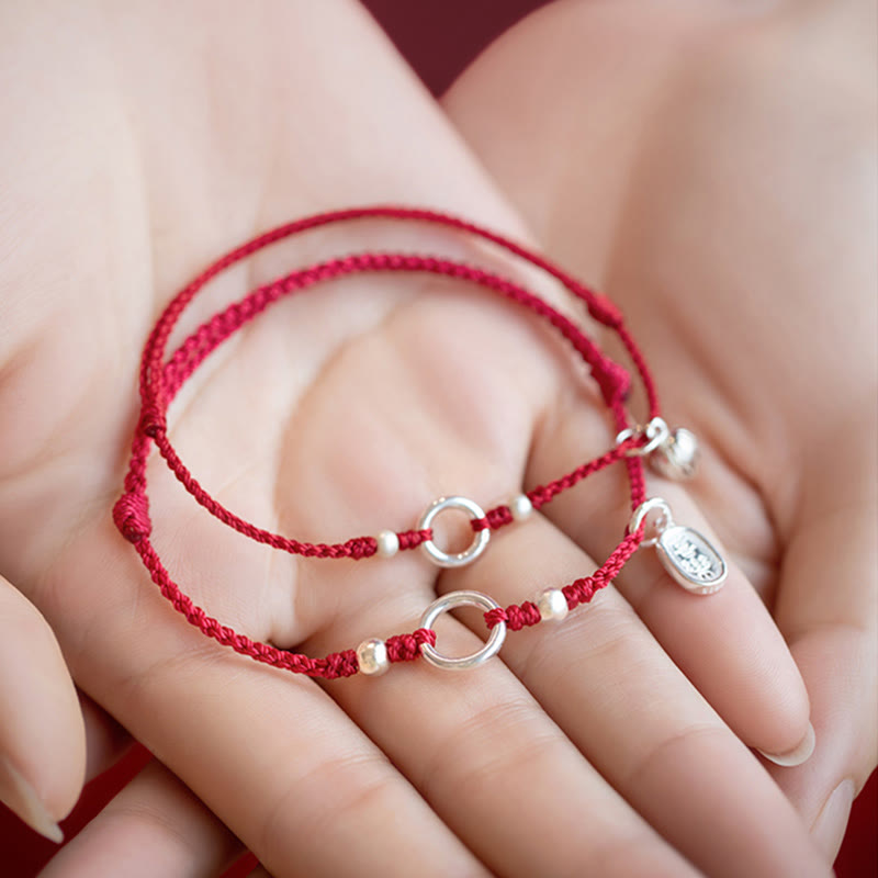 Sterling Silver Lotus Peace Buckle Red String Bracelet – Two red cord bracelets displayed in an open palm showing silver ring centerpieces, spacer beads, and dangling charms