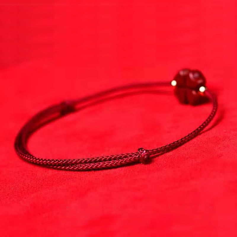 Red braided cord bracelet with cinnabar four leaf clover charm showing heart-shaped lobes gold spacer beads and adjustable knot on vibrant red fabric background