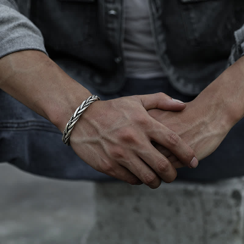 Men's oxidized silver twisted rope cuff bracelet with braided metal design worn on male wrist with dark jacket and gray shirt showing substantial artisan craftsmanship