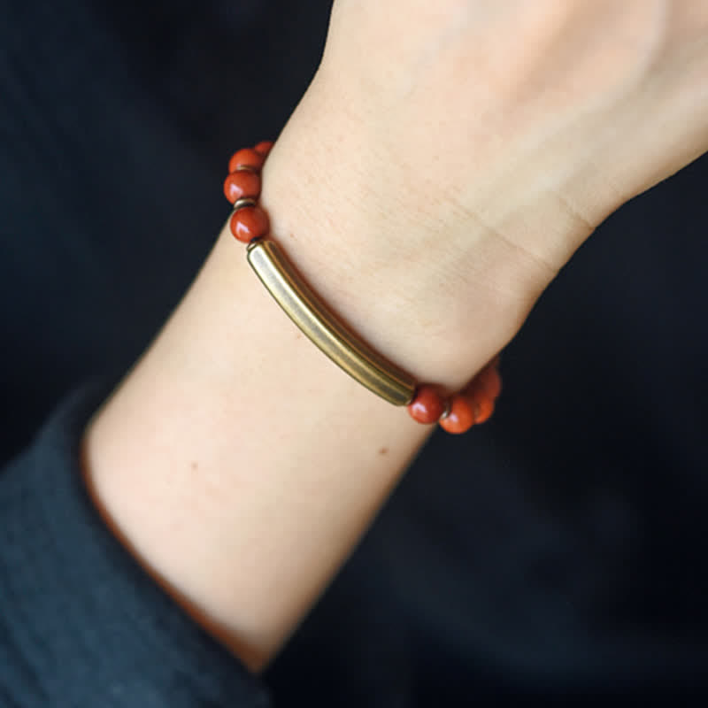 Red jasper bracelet worn on wrist showing terracotta beads with antique bronze curved bar centerpiece, everyday bohemian jewelry lifestyle shot