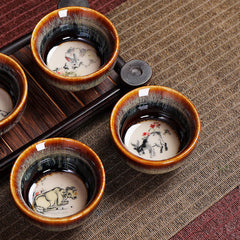 12 Zodiac Jian Zhan Teacup - complete set arrangement showing hare fur glaze cups with zodiac art, woven mat display