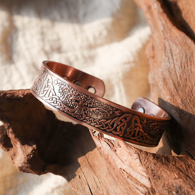 Copper tree of life magnetic therapy cuff bracelet with intricate Celtic knot borders and Norse Yggdrasil engraving displayed on weathered driftwood