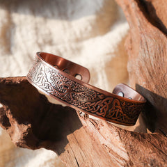 Copper tree of life magnetic therapy cuff bracelet with intricate Celtic knot borders and Norse Yggdrasil engraving displayed on weathered driftwood