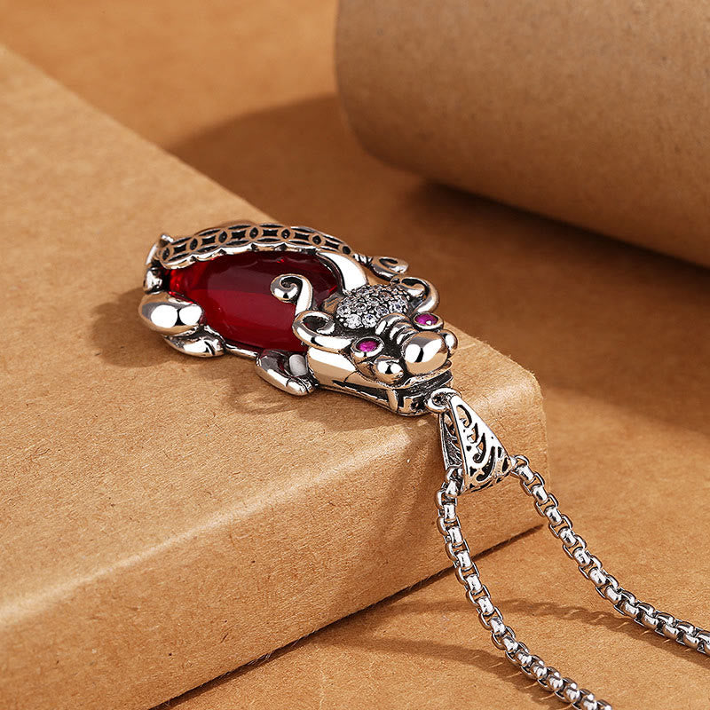 Garnet PiXiu Necklace – PiXiu pendant lying on cardboard block side view with silver chain, luck talisman