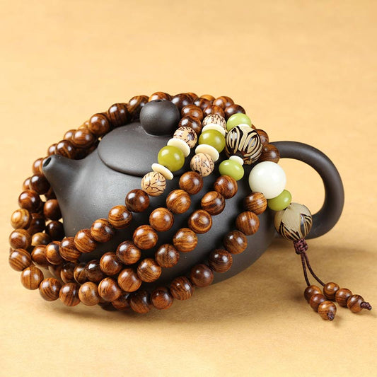 Tibetan Rosewood Bodhi Seed Mala Bracelet draped over black ceramic teapot, green jade and cream spacer beads, carved seed accent beads, traditional 108-bead prayer necklace with tassel, styled product photography