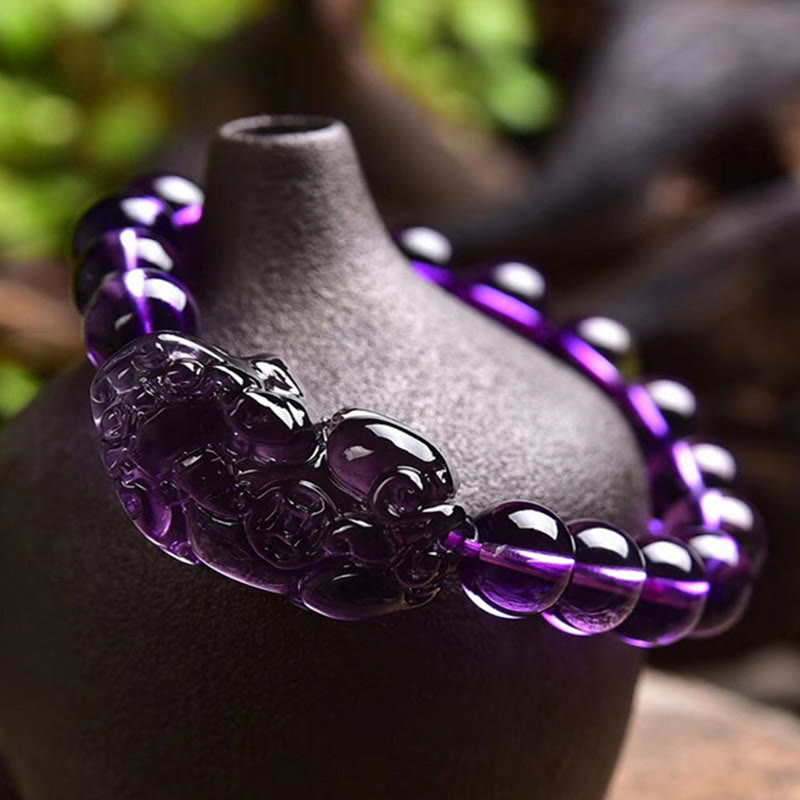 Amethyst PiXiu Fortune Bracelet – Amethyst bracelet draped on black vase, outdoor greenery background