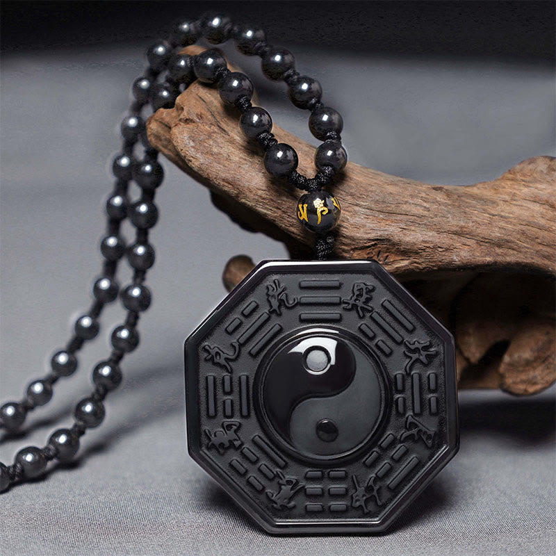 Black Obsidian Yin Yang Pendant Necklace - styled on gray fabric with driftwood, obsidian yin-yang amulet necklace