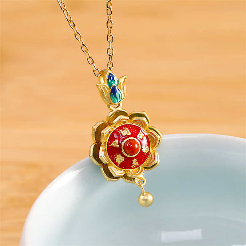 Silver Lotus Prayer Wheel Necklace – gold enamel lotus with red agate center on ceramic display, spiritual