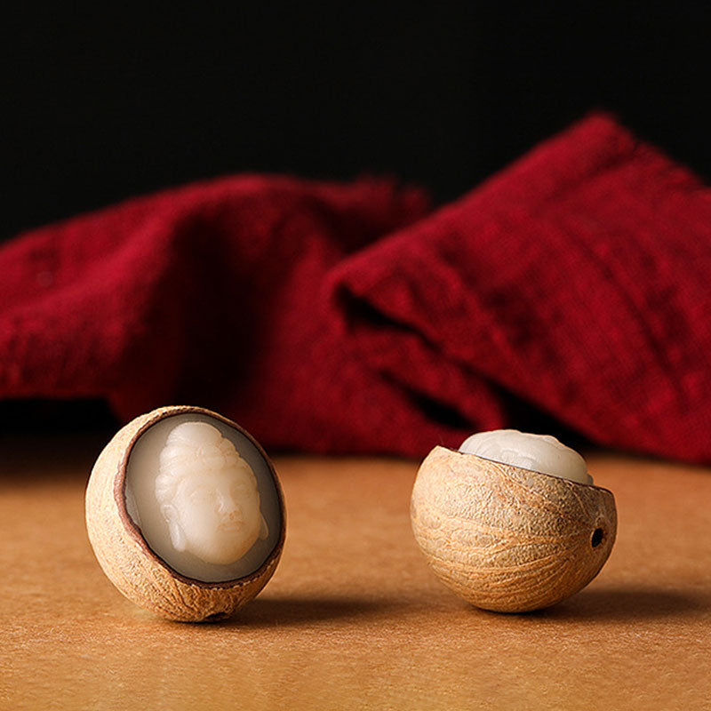 Bodhi Seed Blessing Keychain - two halved bodhi seeds with carved ivory Buddha figures visible inside on crimson fabric, artistry