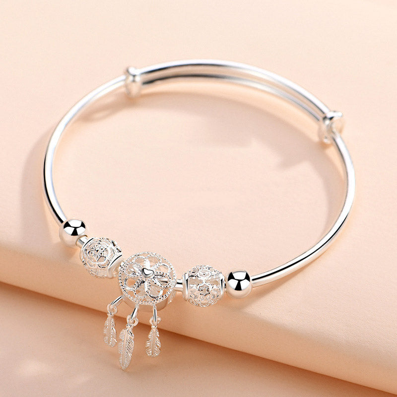 Dream Catcher Blessing Bracelet – Silver bangle on warm peach background showing full charm cluster, product photo