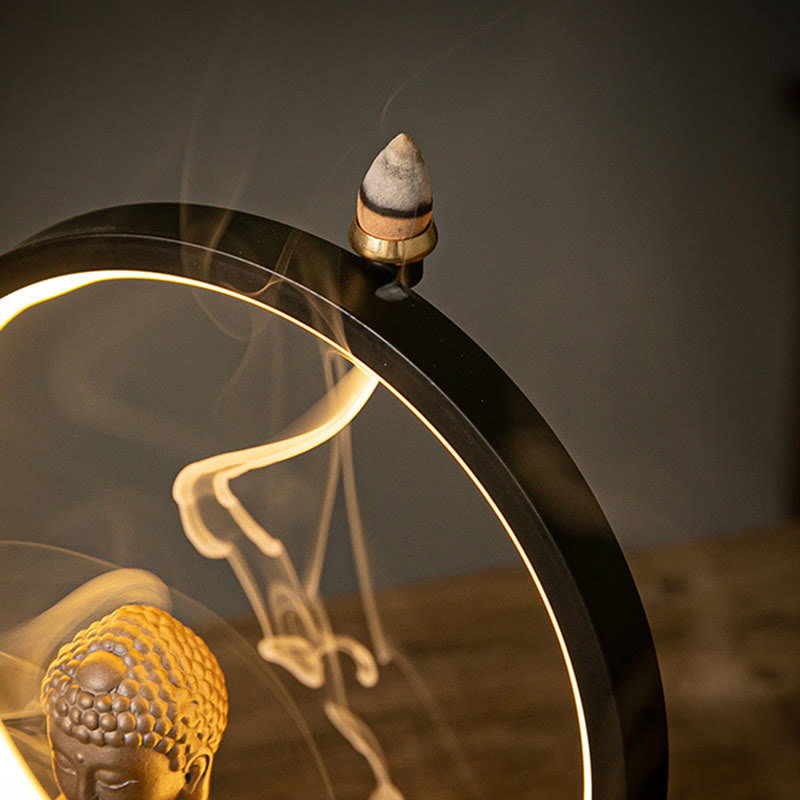 Backflow incense smoke cascading through LED ring with Buddha head below, dramatic warm glow, zen fountain