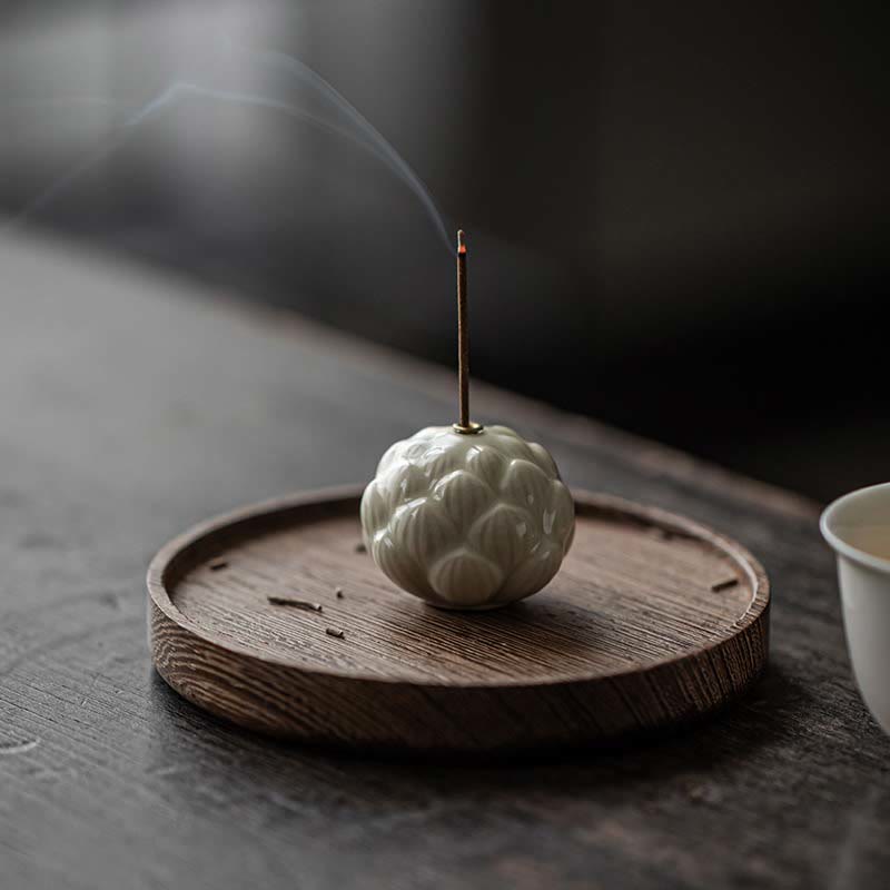 Ceramic Lotus Incense Burner with rising smoke on dark wooden tray, serene