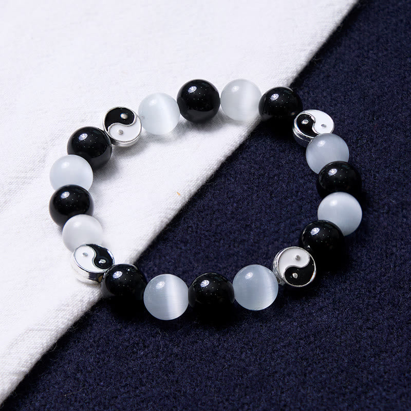 Black Obsidian Cat Eye Yin Yang Bracelet - diagonal view on white and navy fabric, obsidian cat eye yin-yang beaded bracelet