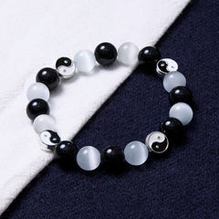 Black Obsidian Cat Eye Yin Yang Bracelet - diagonal view on white and navy fabric, obsidian cat eye yin-yang beaded bracelet