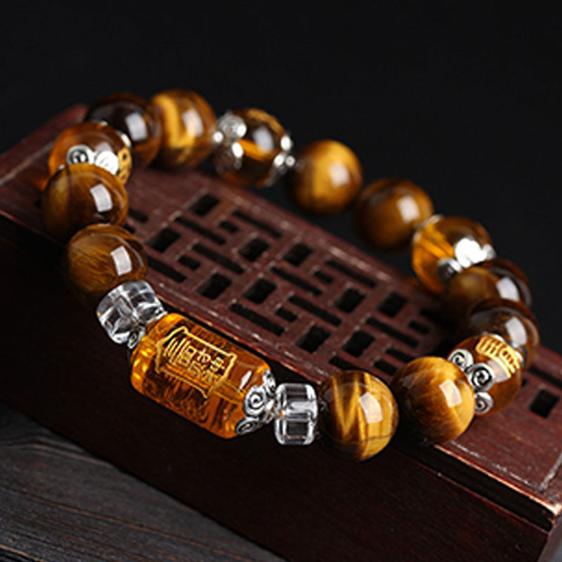 Tiger eye gemstone bracelet with amber barrel bead engraved with fortune Fu character and ornate silver metal caps on carved wooden lattice stand, dark background