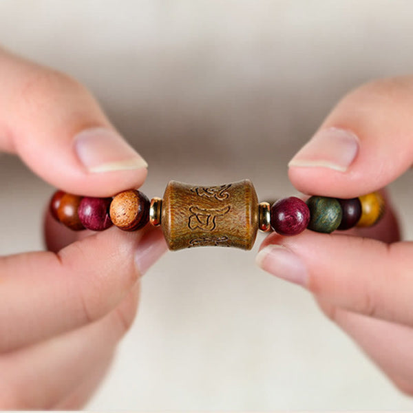 Multicolored Sandalwood Prayer Bracelet – Hand-held presentation showing carved center bead, wooden mala