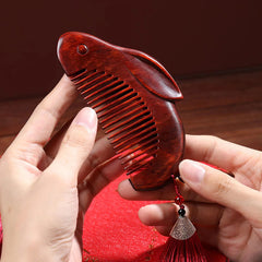 Hands holding cute bunny-shaped red sandalwood massage comb with red tassel