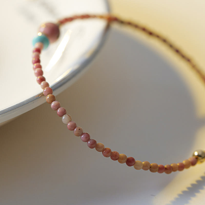 Rhodonite Loving Energy Bracelet – Pink beads with rose focal and turquoise accent worn on wrist, white background close-up side view with hand
