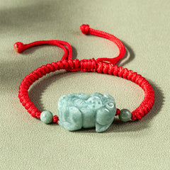 Jade PiXiu Knot Bracelet – Red braided cord bracelet with light green jade PiXiu on beige surface, protection jewelry