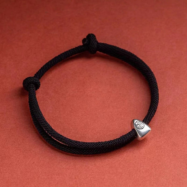 925 Silver Fu Character Braided Bracelet – Black braided cord with silver fortune charm on terracotta orange textured background, overhead flat lay product shot