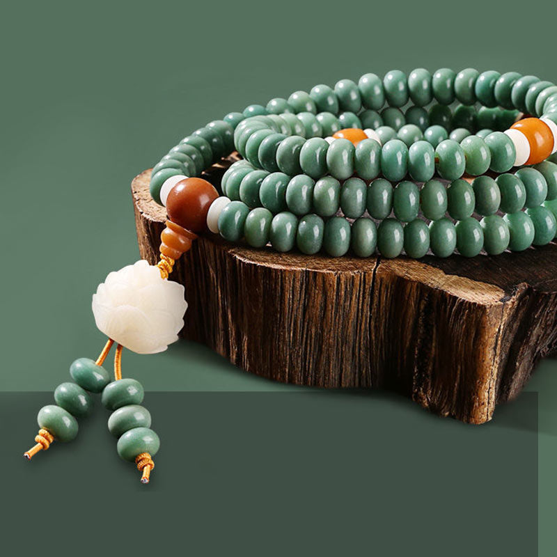 Lotus Cyan Bodhi Seed Bracelet - sage mala coiled on wood slice with amber accents and lotus pendant, green backdrop
