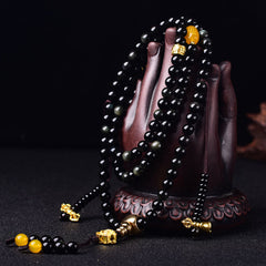 Black Obsidian Lotus Mala Bracelet - Draped over carved Buddha hand on black, gold lotus pendant, obsidian mala