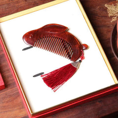 Bunny-shaped red sandalwood comb lying inside open red gift box with tassel