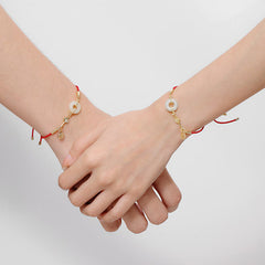 Matching couple red cord bracelets with white jade peace buckle pendants, gold chain details and crystal accents on clasped hands, white background