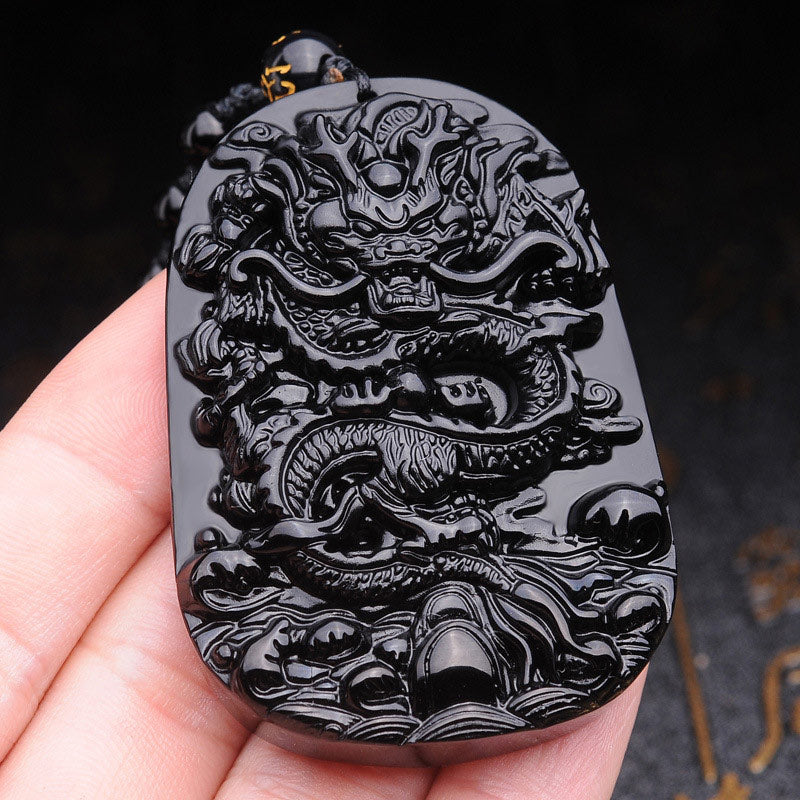 Black Obsidian Dragon Pendant – Hand-held close-up of carved dragon relief, grounding