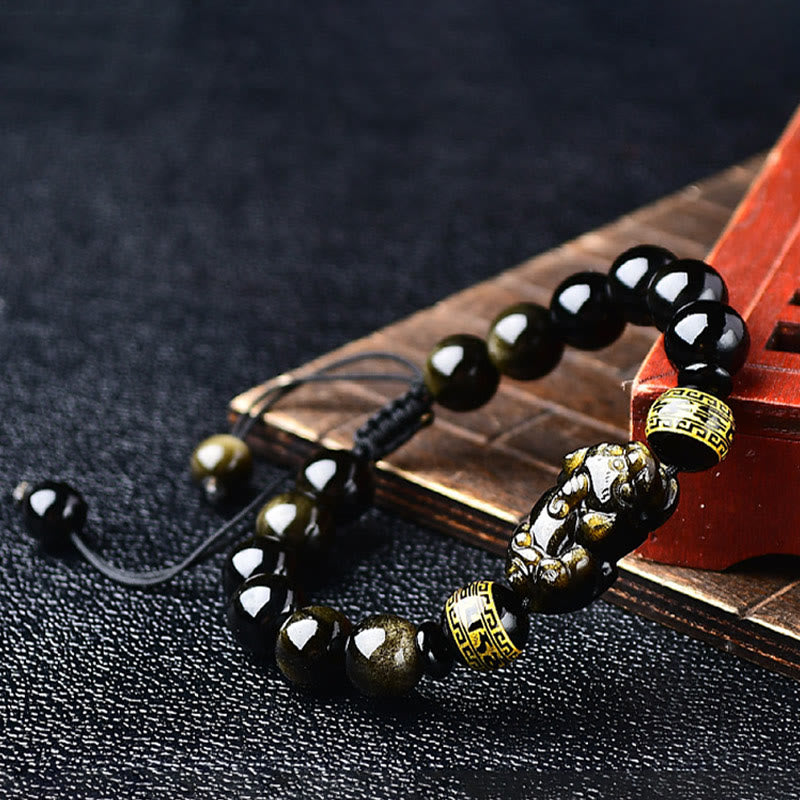 Gold Sheen Obsidian Pixiu Bracelet – Diagonal view on dark fabric with carved wood prop, wealth charm