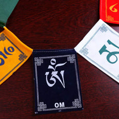 Tibetan Prayer Flags – Overhead flat lay on dark wood showing Om Mani Padme Hum mantra and endless knot borders