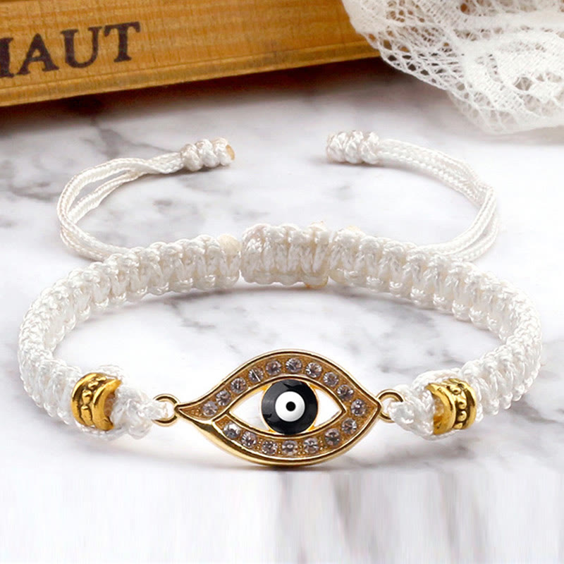 White cord evil eye bracelet with gold crystal evil eye charm on white marble styling