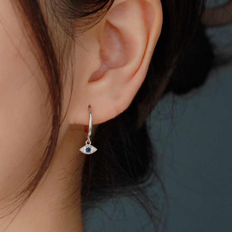 Evil Eye Huggie Hoop Earring Worn on Ear with Gray Bokeh Background, Silver Protection