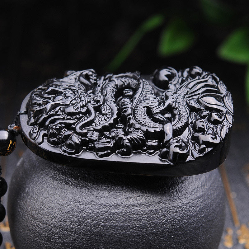Black Obsidian Dragon Pendant – Low-angle dragon carving on black ceramic with greenery, powerful