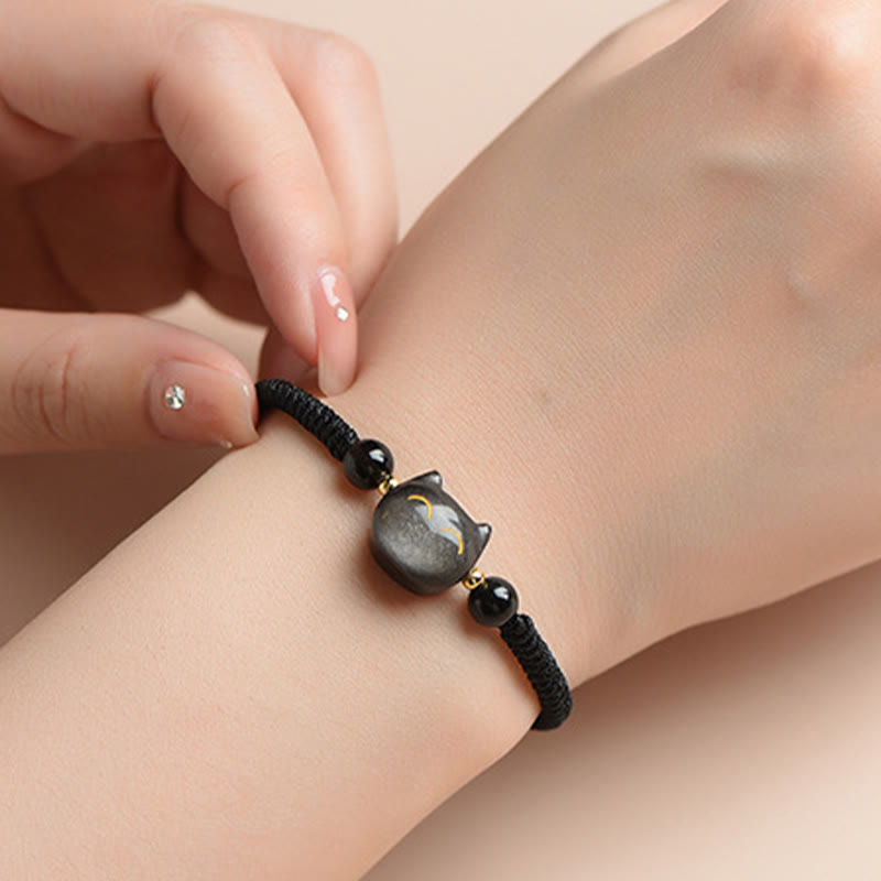 Black woven cord bracelet with obsidian cat charm and gold accents worn on wrist, handmade adjustable cat protection jewelry for women