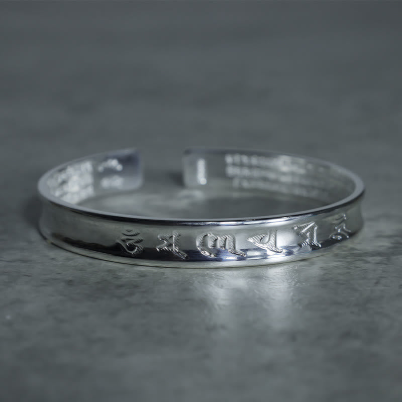 Tibetan Mantra Copper Bracelet - Raised Tibetan script on broad open cuff, textured gray backdrop