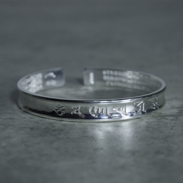 Tibetan Mantra Copper Bracelet - Raised Tibetan script on broad open cuff, textured gray backdrop