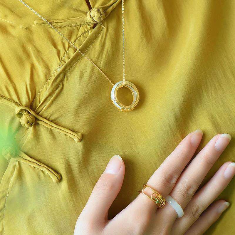 White Jade Luck Ring Necklace – Gold chain necklace with white jade ring pendant worn with matching jade and filigree rings on mustard-yellow traditional Chinese garment