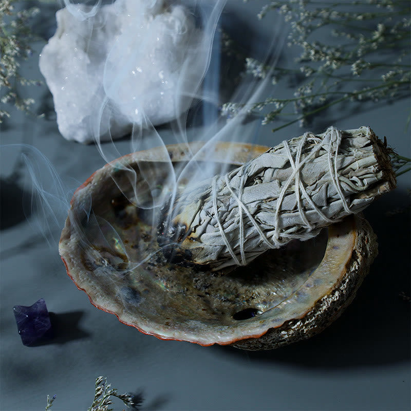 Burning sage smudge stick in abalone shell with quartz and dried flowers